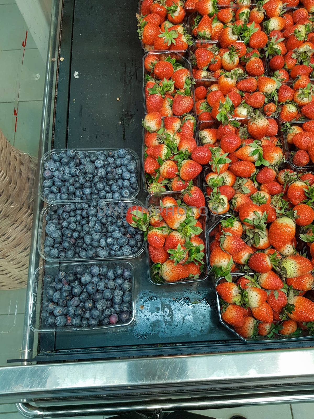 Lots of blueberries and strawberries in containers on the counter in the store, close-up, vertical.