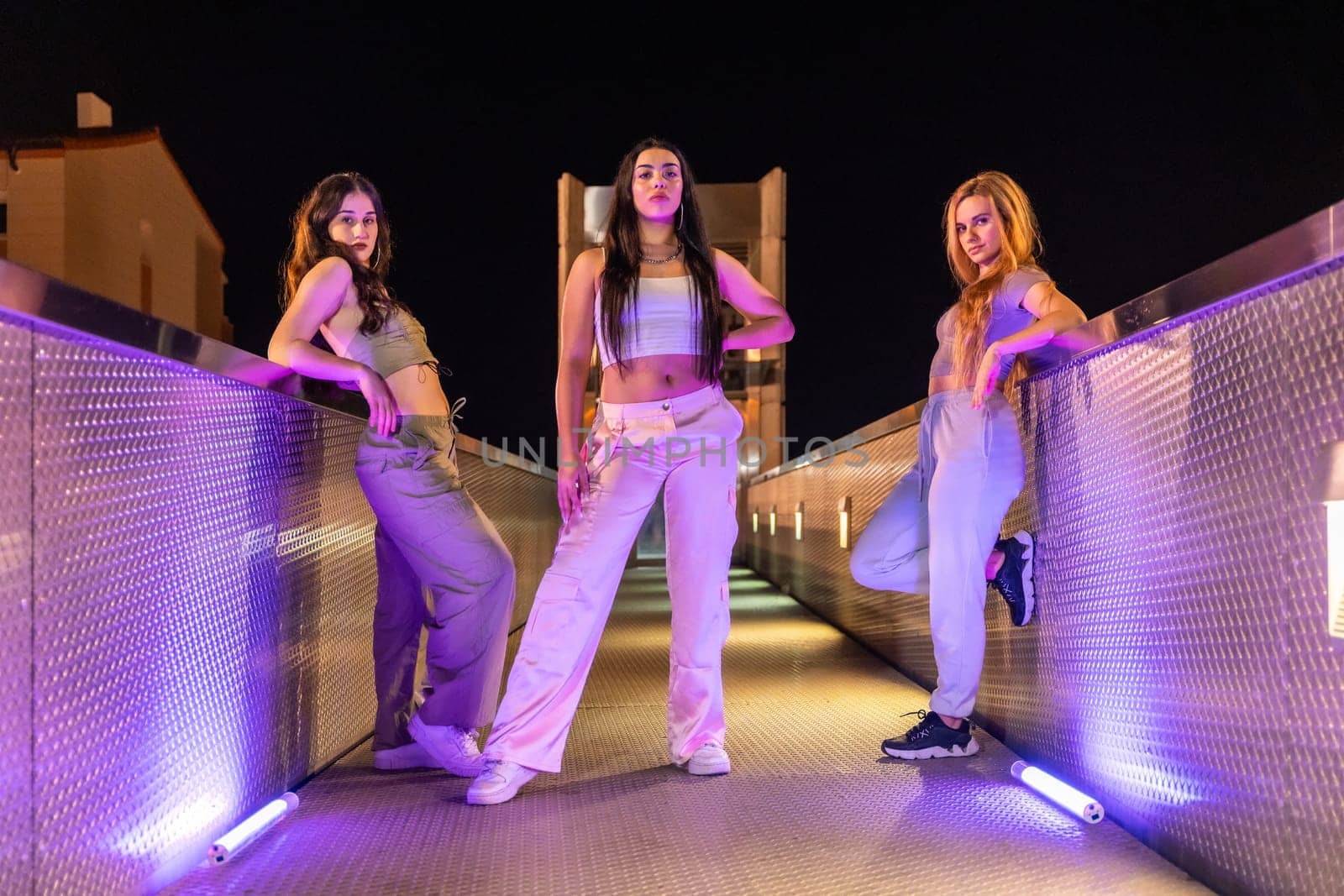 Street dancers are dancing in the middle of a bridge with neon lights at night