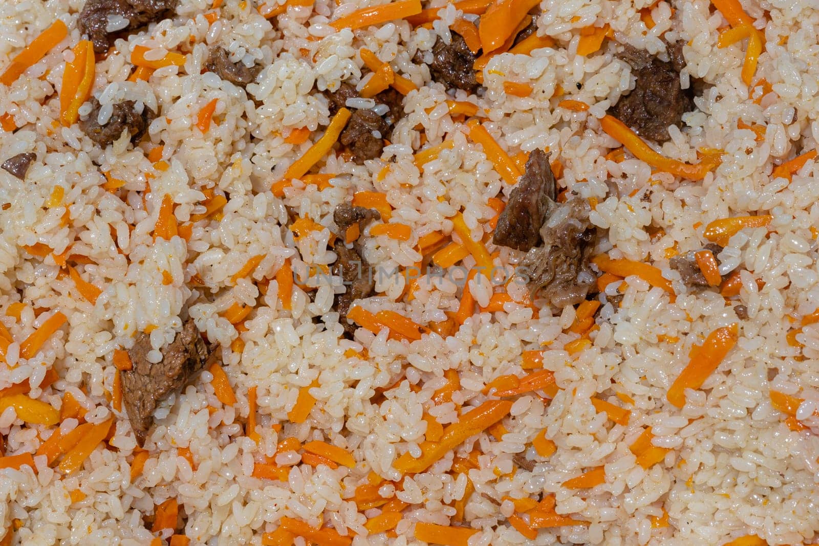 Close-up view of Asian tasty food background. Traditional Eastern culinary dish - pilaf. Ingredients: rice with slices of meat, fat and vegetables carrot, garlic, spices - popular recipe.