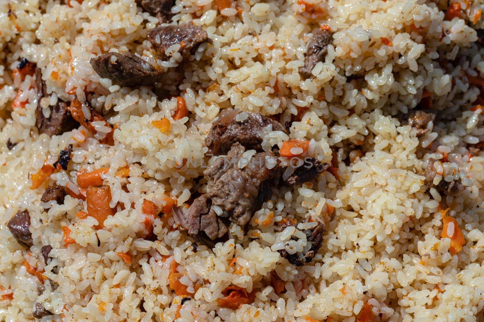 Traditional Eastern culinary dish - pilaf. Ingredients: rice with slices of meat, fat and vegetables (carrot, garlic), spices - popular recipe. Close-up view of Asian tasty food background.