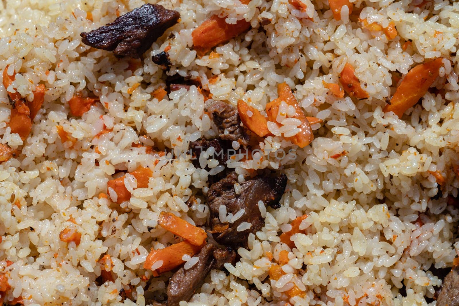Closeup view of Eastern tasty food background. Traditional Asian culinary dish - pilaf. Ingredients: rice with slices of meat, fat and vegetables (carrot, garlic), spices - popular recipe.
