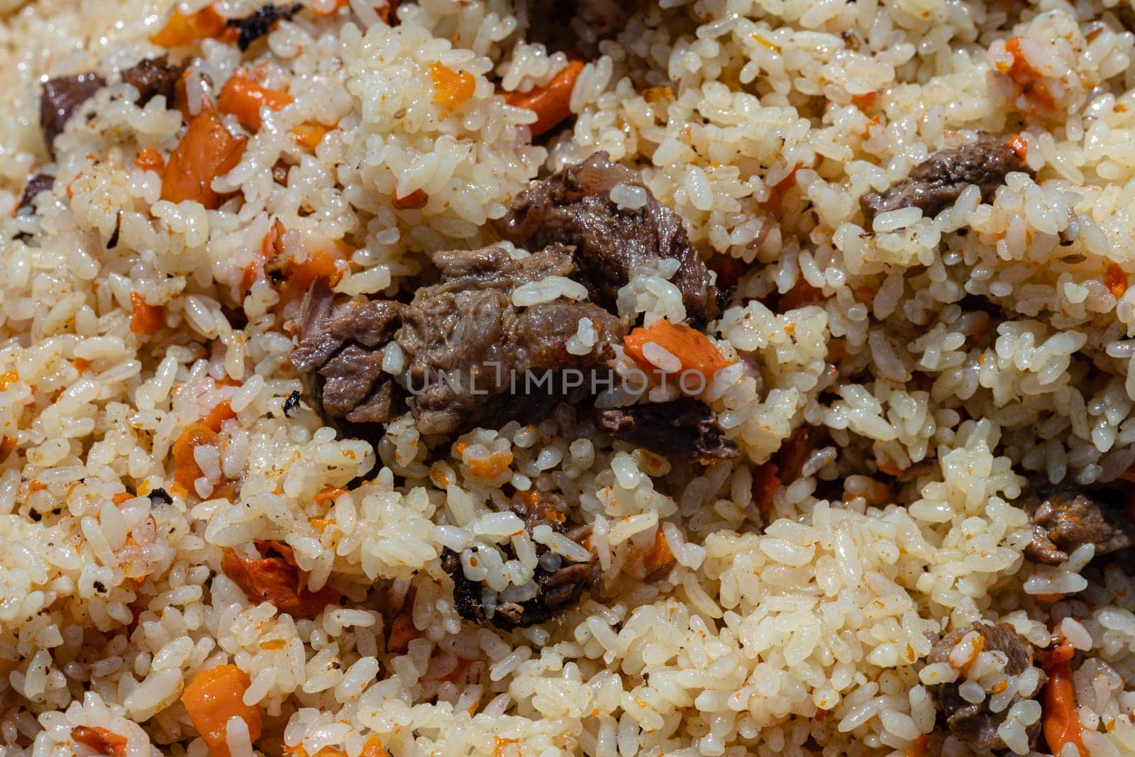 Close-up view of Asian tasty food background. Traditional Eastern culinary dish - pilaf. Ingredients: rice with slices of meat, fat and vegetables (carrot, garlic), spices - popular recipe.