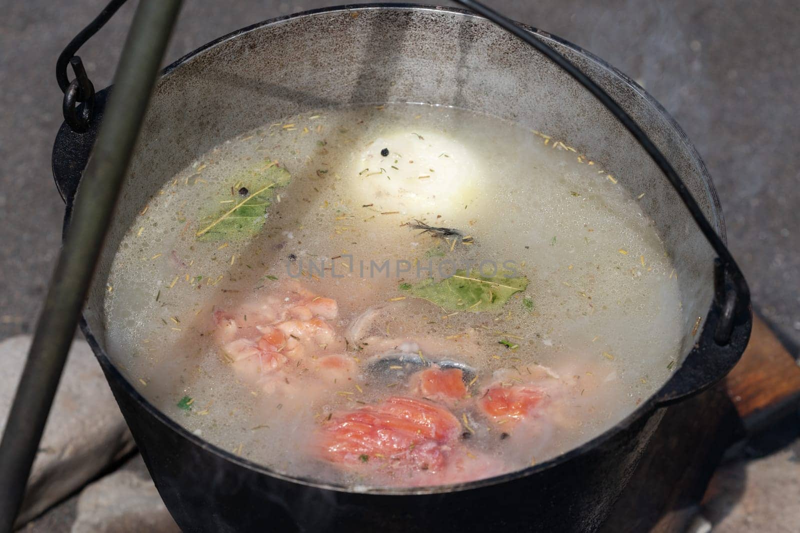 Delicious red salmon fish fresh-soup cooked in large bowler on campfire outdoors. Cooking food on fire during picnic on sunny summer day.