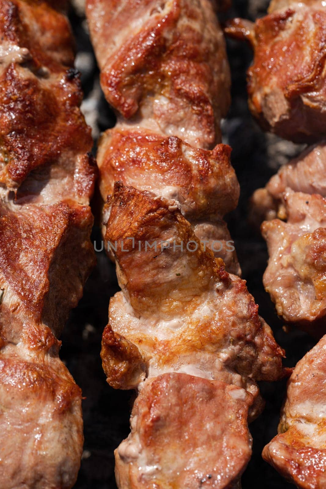 Appetizing juicy pork shish kebabs cooking on metal skewers on charcoal grill with fragrant smoke. Closeup view, selective focus on tasty pieces of roast meat. Cooking during summer picnic.