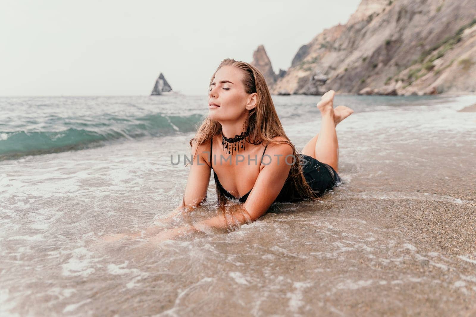 Woman travel sea. Young Happy woman in a long red dress posing on a beach near the sea on background of volcanic rocks, like in Iceland, sharing travel adventure journey