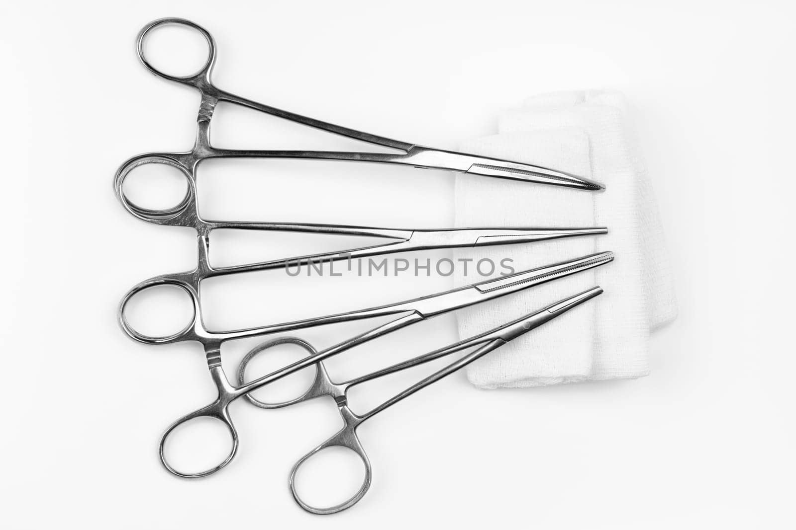 Lot of stainless surgical needle drivers lying on white sterile gauze swab. Medical instruments needle holders on white background. Healthcare and medicine concept. Flat shot, selective focus