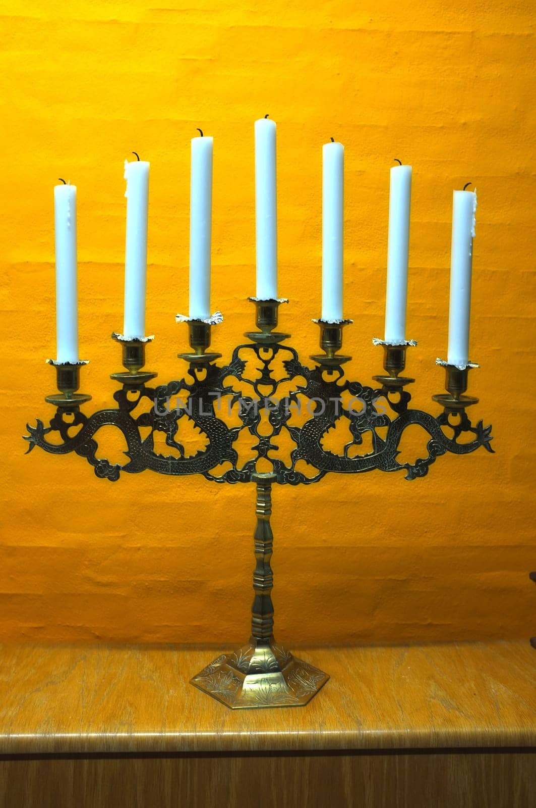 Candle, vintage and holder in church on table at interior of room or cathedral. Wax, brass and retro candlestick for decoration at temple, wood and copper metal with antique candelabra for lighting by YuriArcurs