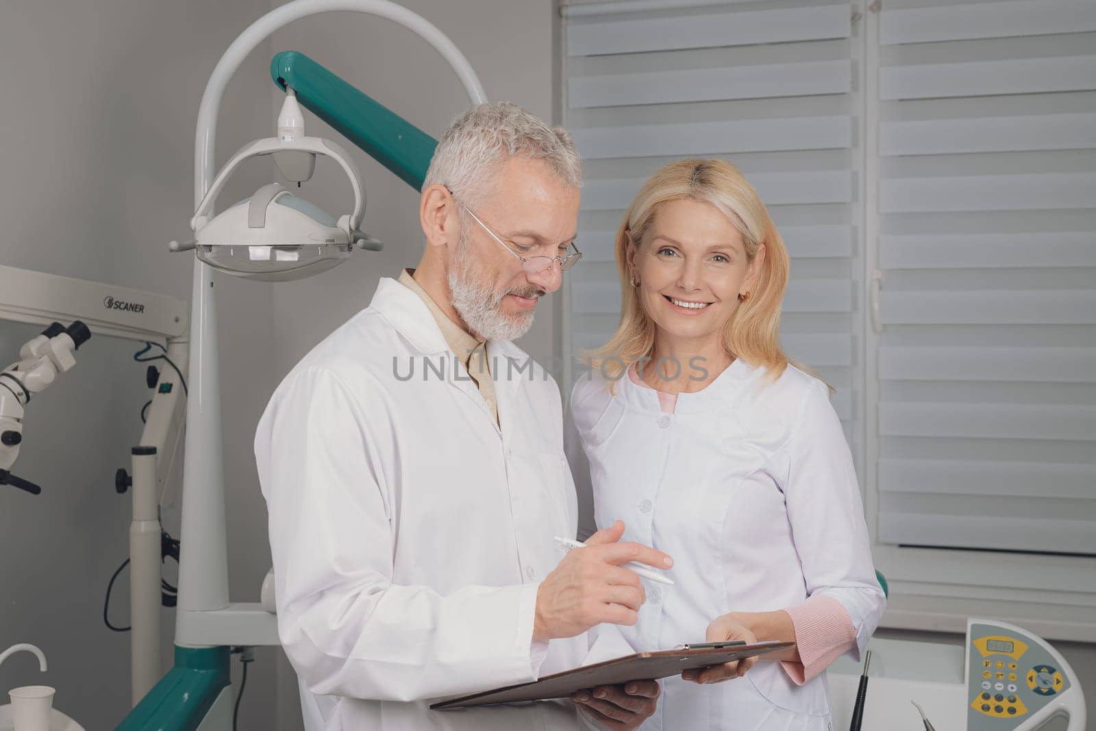 Male and female dental doctors wearing face sitting at his clinic. by Сookiestock