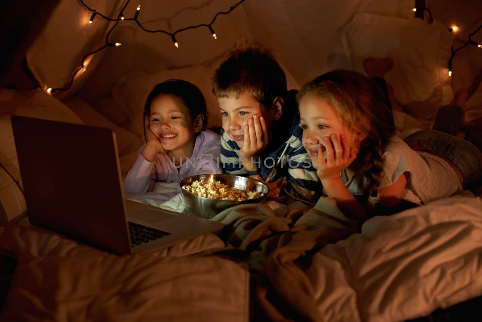 Children, computer and watch in tent at night with movies, film or cartoons for holiday adventure or vacation. Young boy, girl or kids with lights, pillows and blanket at home on laptop for Netflix.