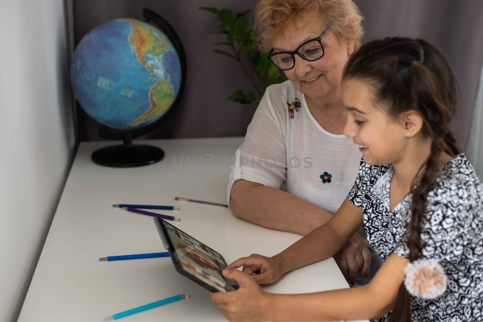 Happy mature grandmother with adorable little granddaughter using tablet at home together, excited middle aged woman and cute kid looking at device screen by Andelov13