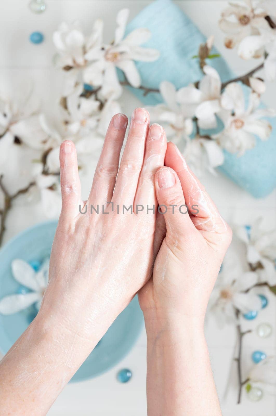 young woman doing step by step hand massage with cream in salon with cup of spring water and blue spa stones and white magnolia flowers, High quality photo