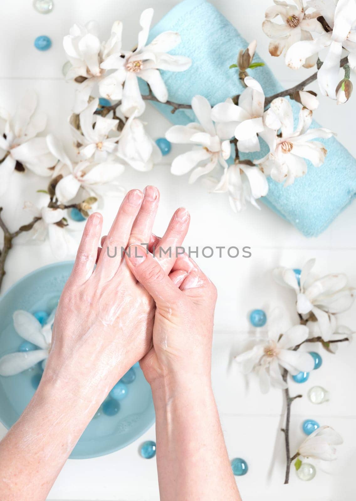 young woman doing step by step finger massage with cream in salon with cup of spring water and blue spa stones and white magnolia flowers, High quality photo