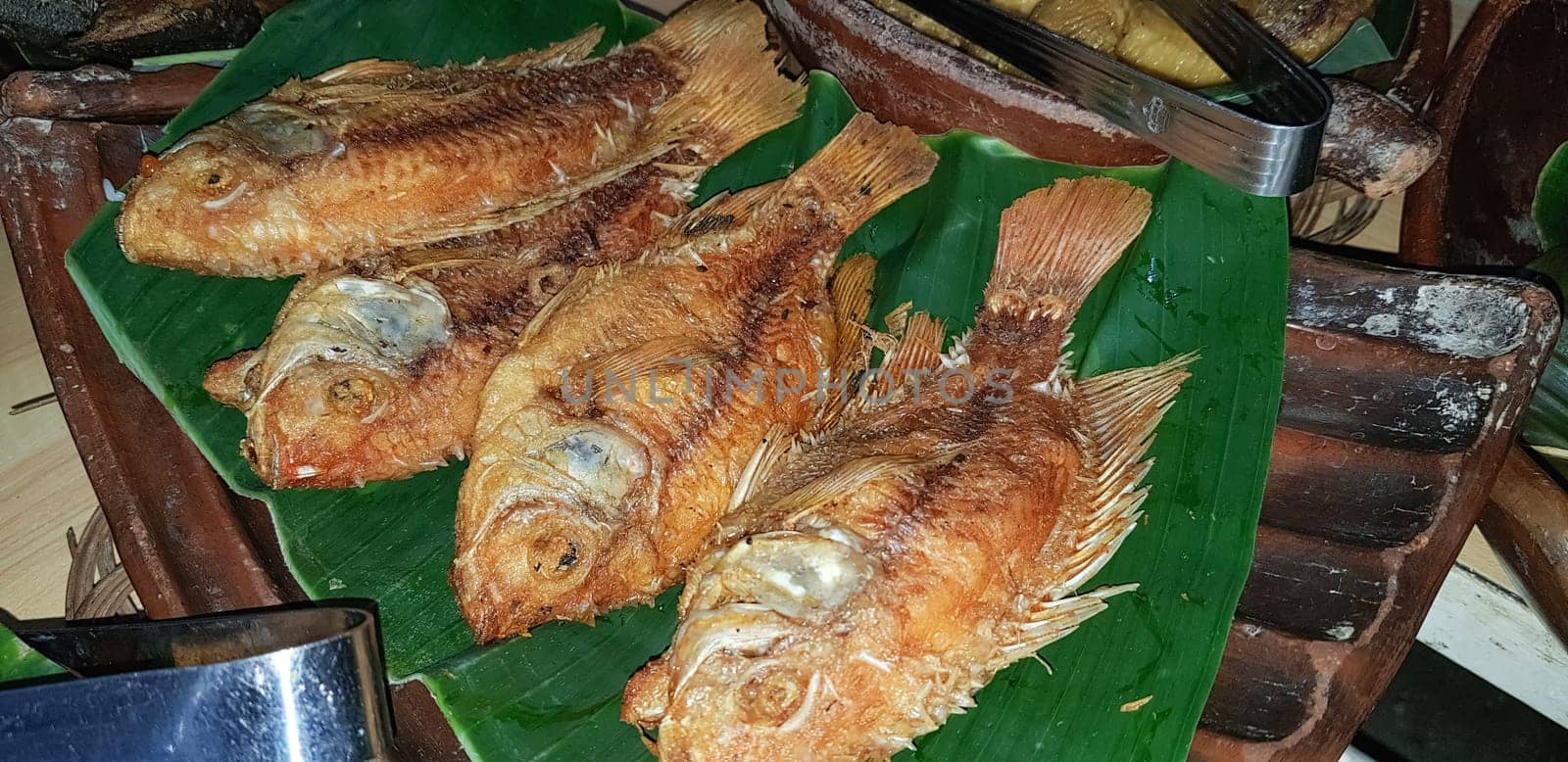 Seafood dish served on the table and plate from above with different kind of dish from fried fish barracuda, snapper, tuna jaws, and also mix of tropical vegetables and sambal or chili paste