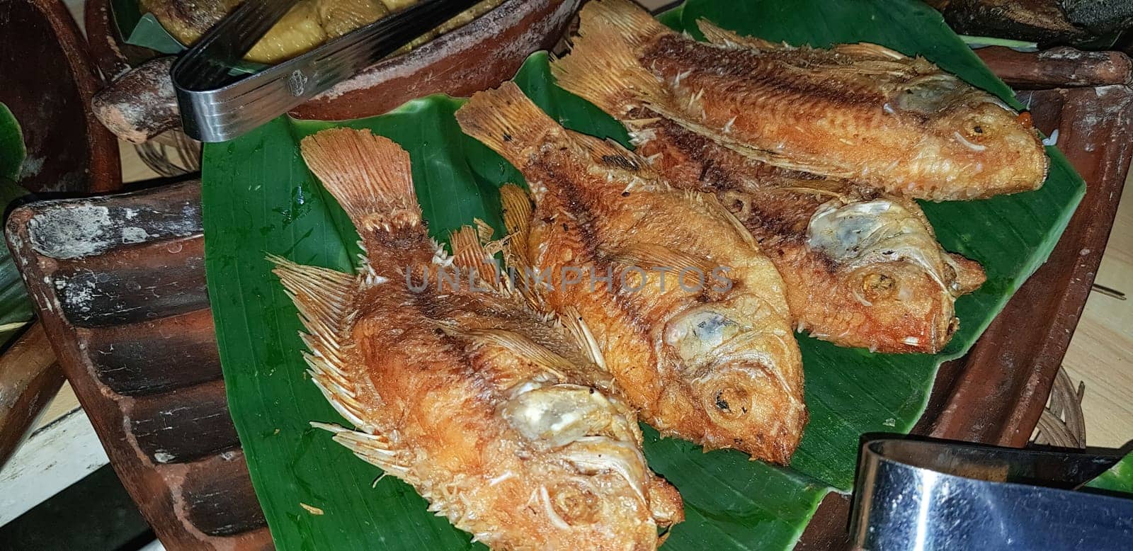 Seafood dish served on the table and plate from above with different kind of dish from fried fish barracuda, snapper, tuna jaws, and also mix of tropical vegetables and sambal or chili paste