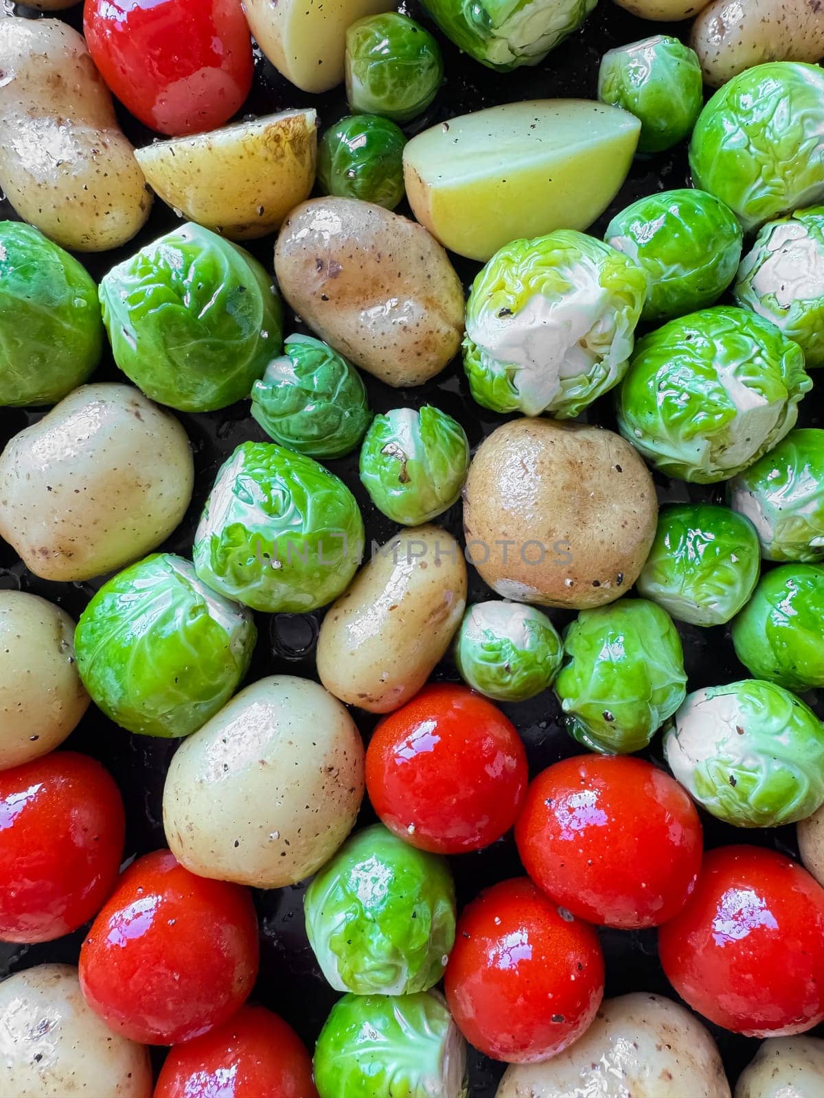 Close up of raw baby potatoes, Brussels sprouts, and cherry tomatoes prepared for roasting, colorful fresh ingredients concept. by Lunnica