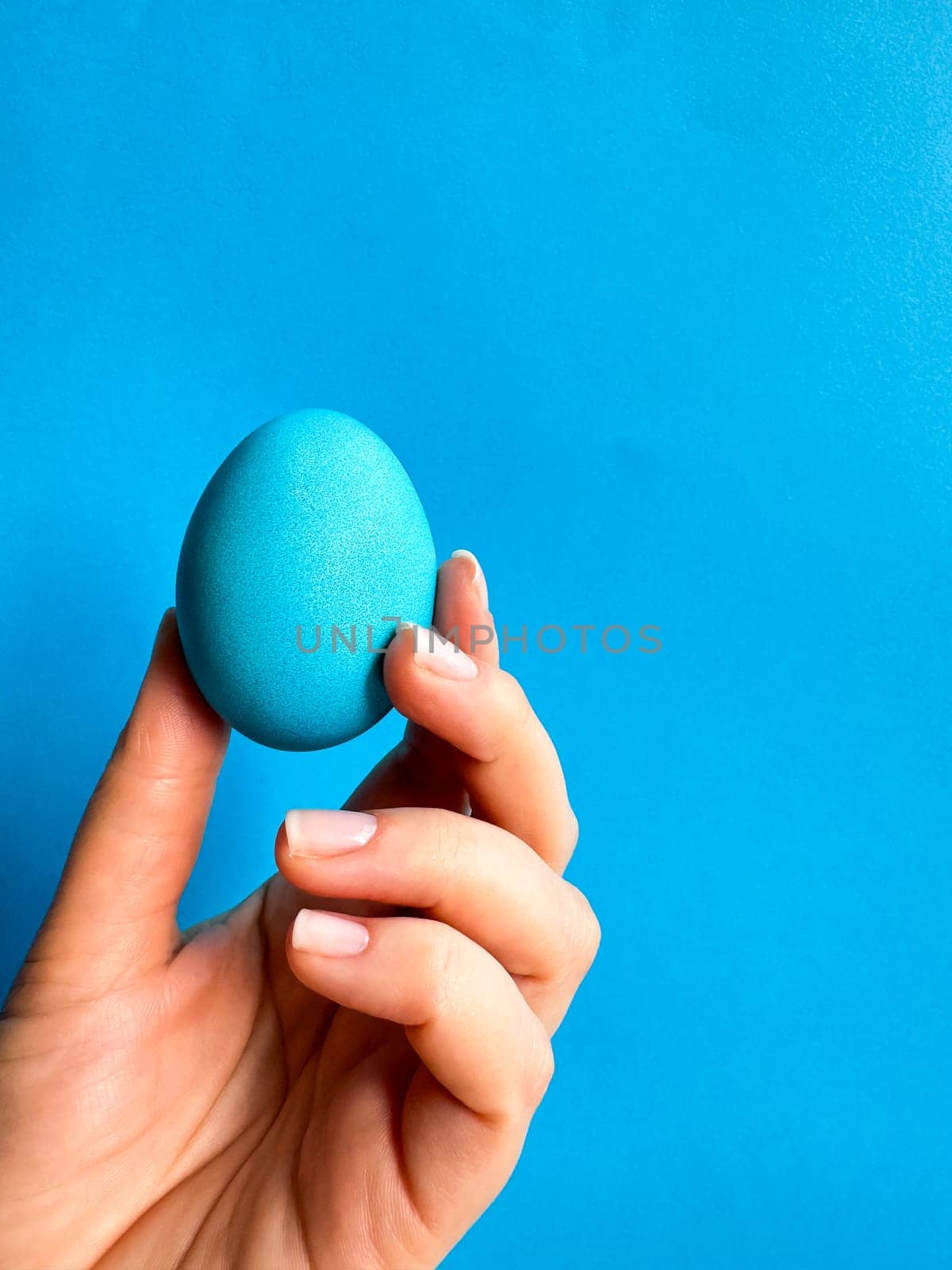 Hand balancing blue egg on a fingertip against solid blue background, minimalist concept for balance, Easter, and simplicity with space for text. by Lunnica