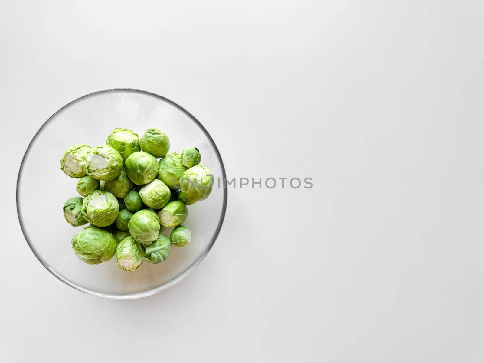 Brussels sprouts in transparent glass bowl on white background with ample space for text, healthy food concept. by Lunnica