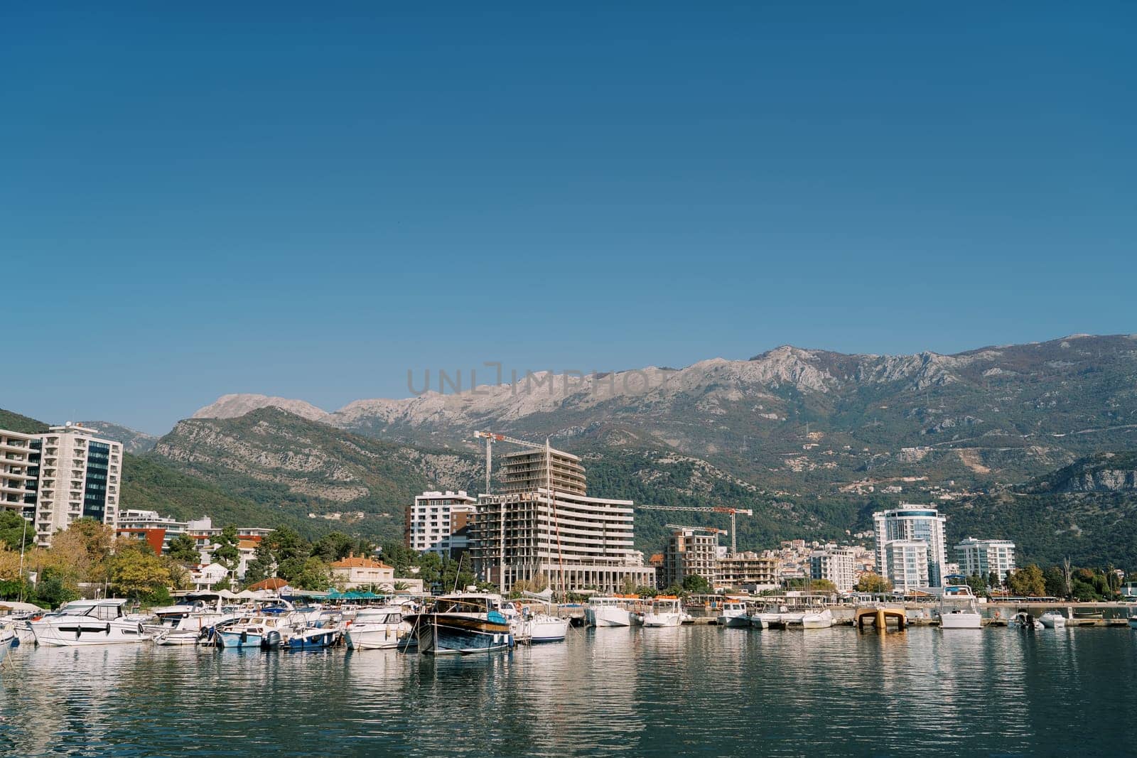 Motorboats along the shore of Budva and residential buildings under construction at the foot of the mountains. Montenegro. High quality photo