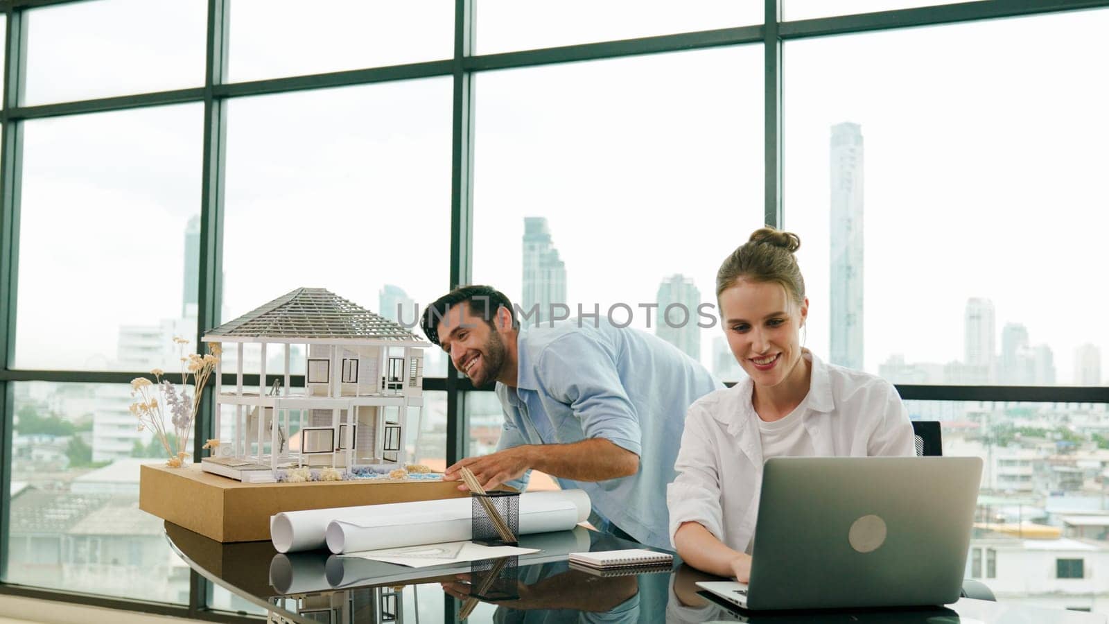 Smart architect engineer inspect house model while colleague using laptop analysis data. Professional designer team working together to design house model construction at modern office. Tracery