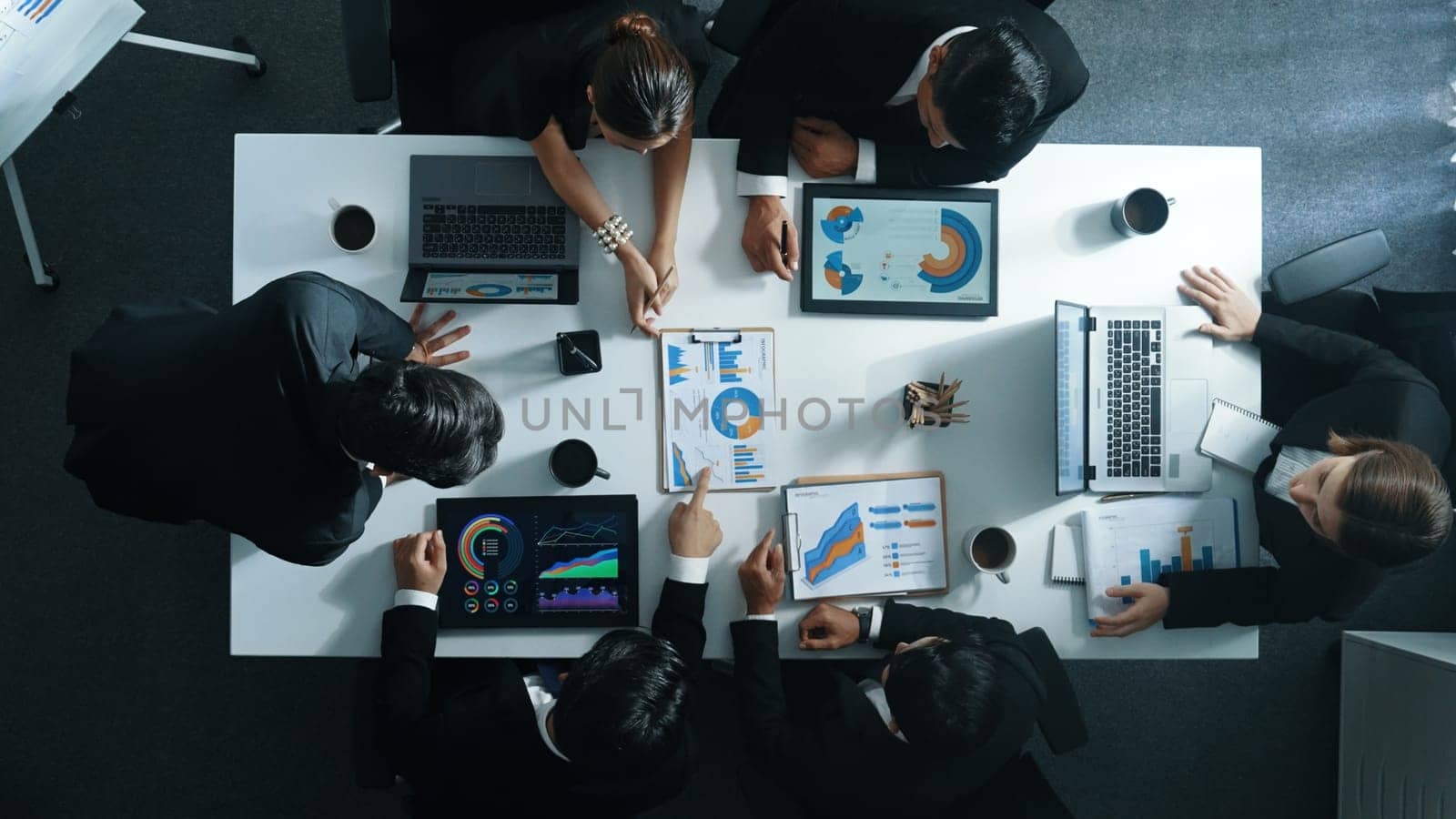 Top down aerial view of business people discussing about financial strategy on table with document and tablet display investment statistic at meeting. Diverse team brainstorm about plan. Directorate.