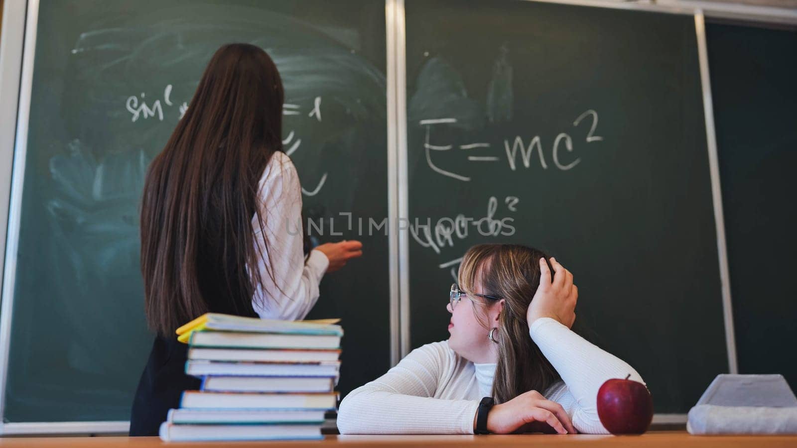 Two high school girls at the blackboard in their class. by DovidPro