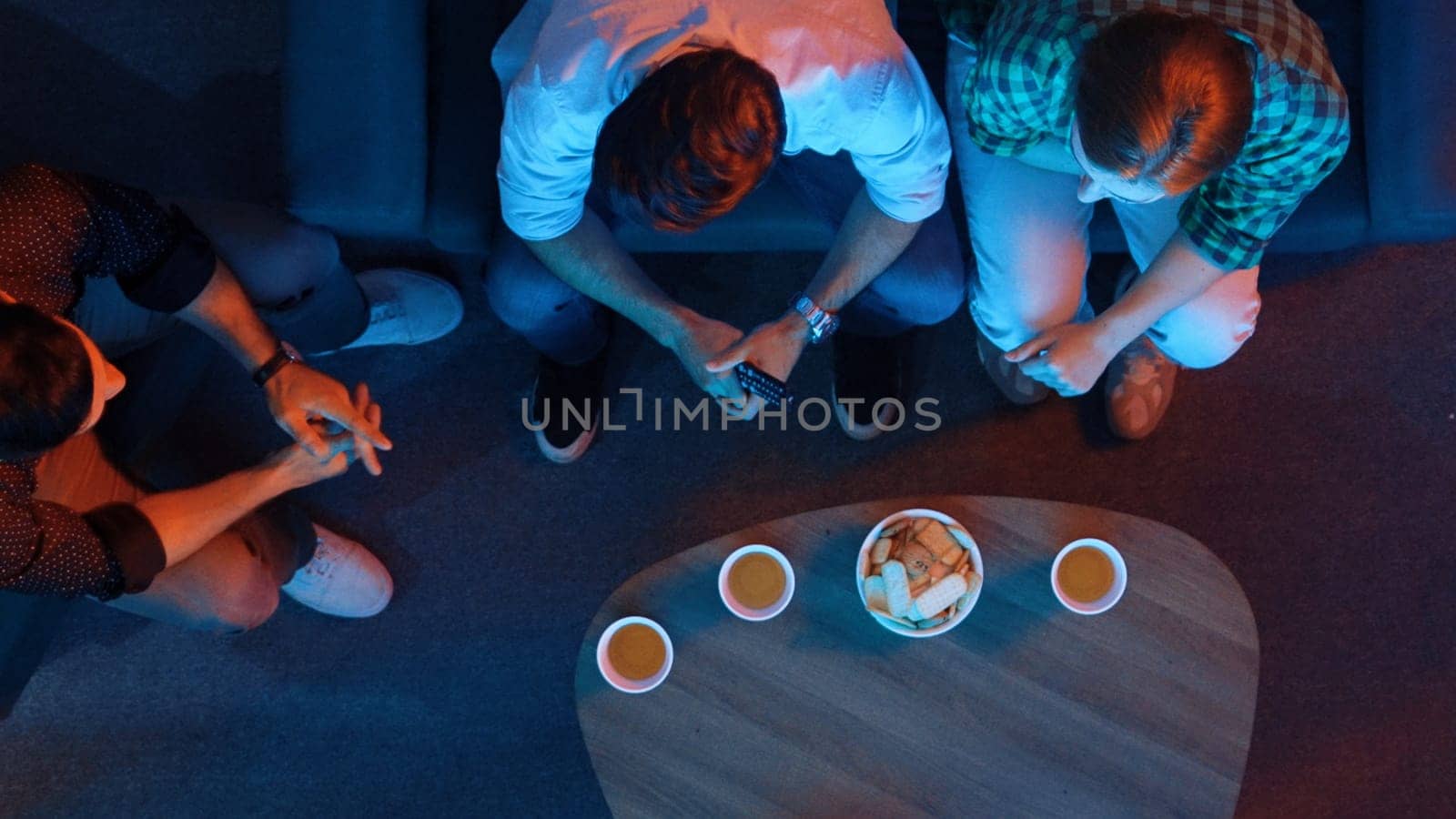 Happy family and colleague sitting at dark living room with red filter while cheering football team together. Caucasian people enjoy watching tv and giving high five and clinking glasses. Convocation.