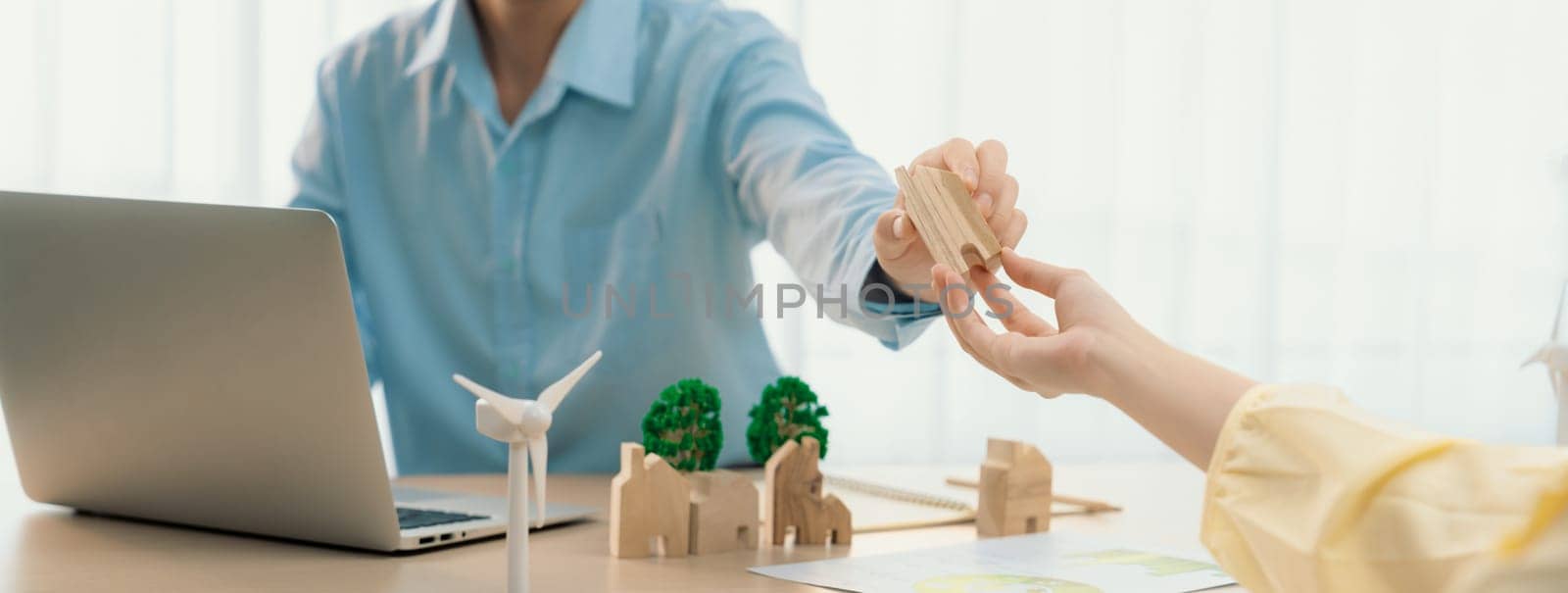 Two business people talking about eco city at green business meeting on meeting table with windmill represented renewable energy, wooden house block and tree model represent green city. Delineation.