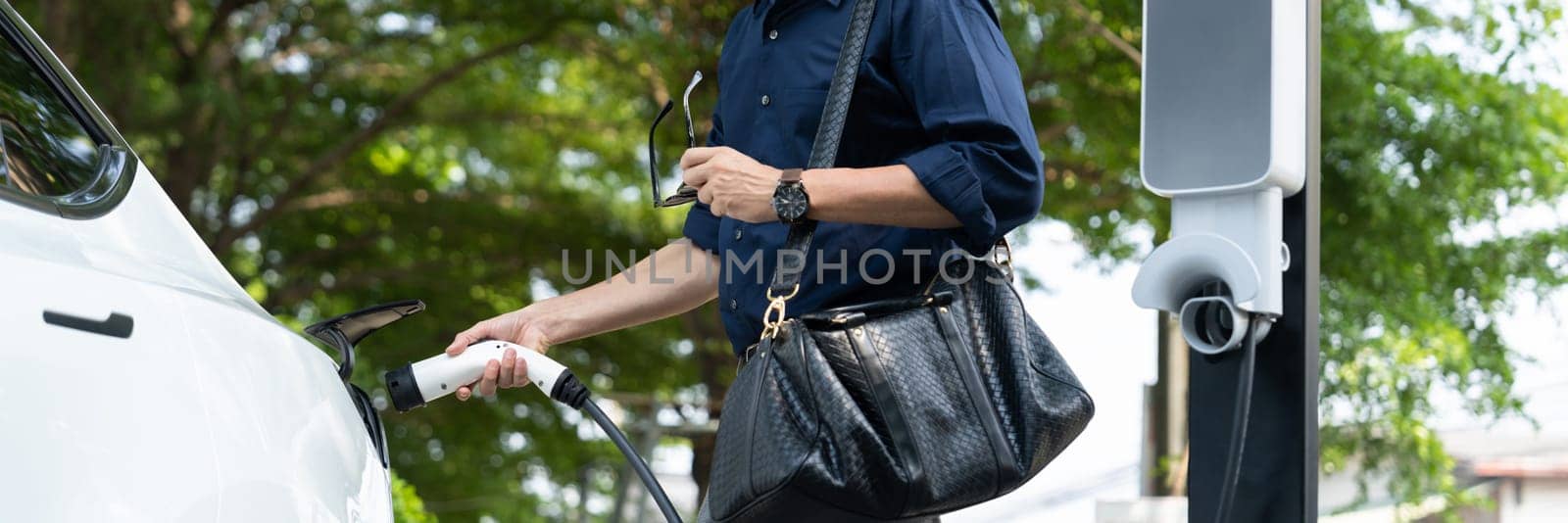 Young man recharge electric car's battery from charging station. Expedient by biancoblue