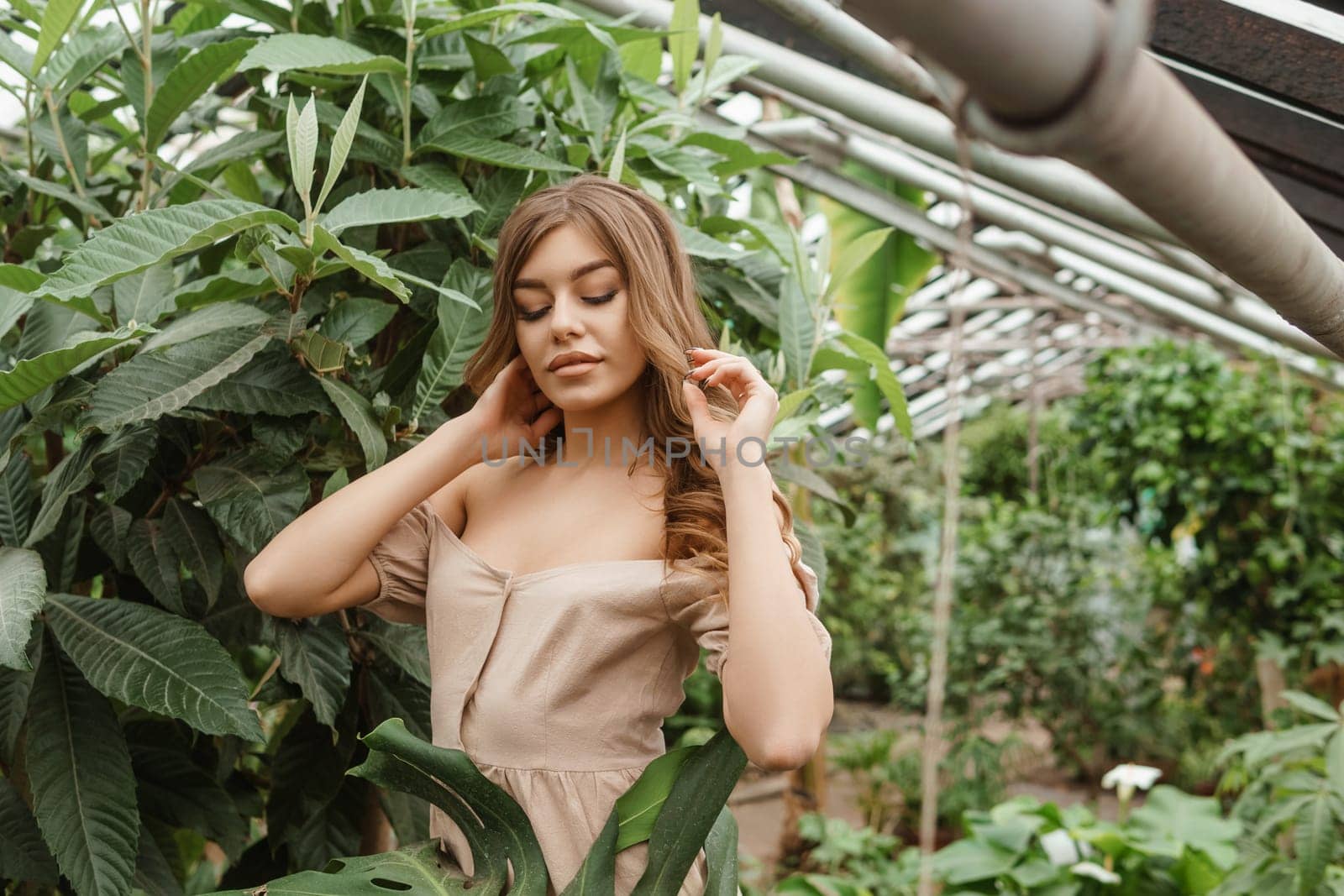 A beautiful young woman takes care of plants in a greenhouse. The concept of gardening and an eco-friendly lifestyle