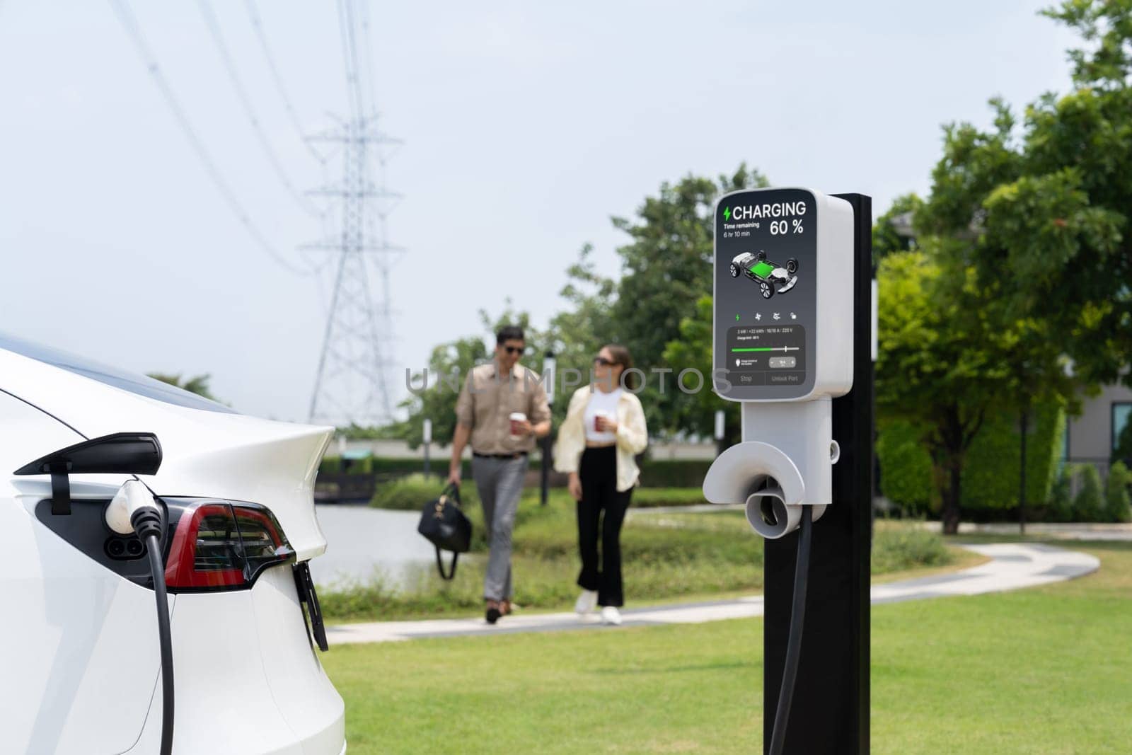 Young couple with coffee recharge EV car battery at charging station connected to electrical industrial power grid tower. Couple with shopping and travel using eco electric car lifestyle. Expedient