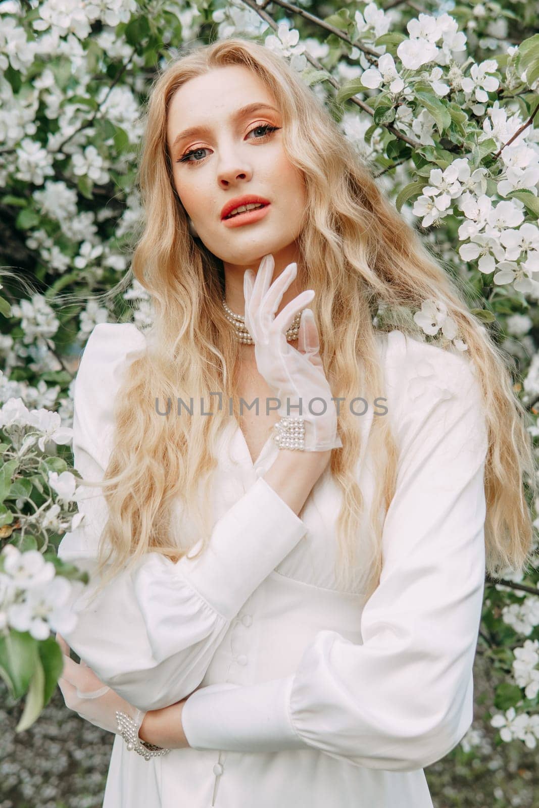 A blonde girl with long hair on a walk in a spring park. Springtime and blooming apple trees