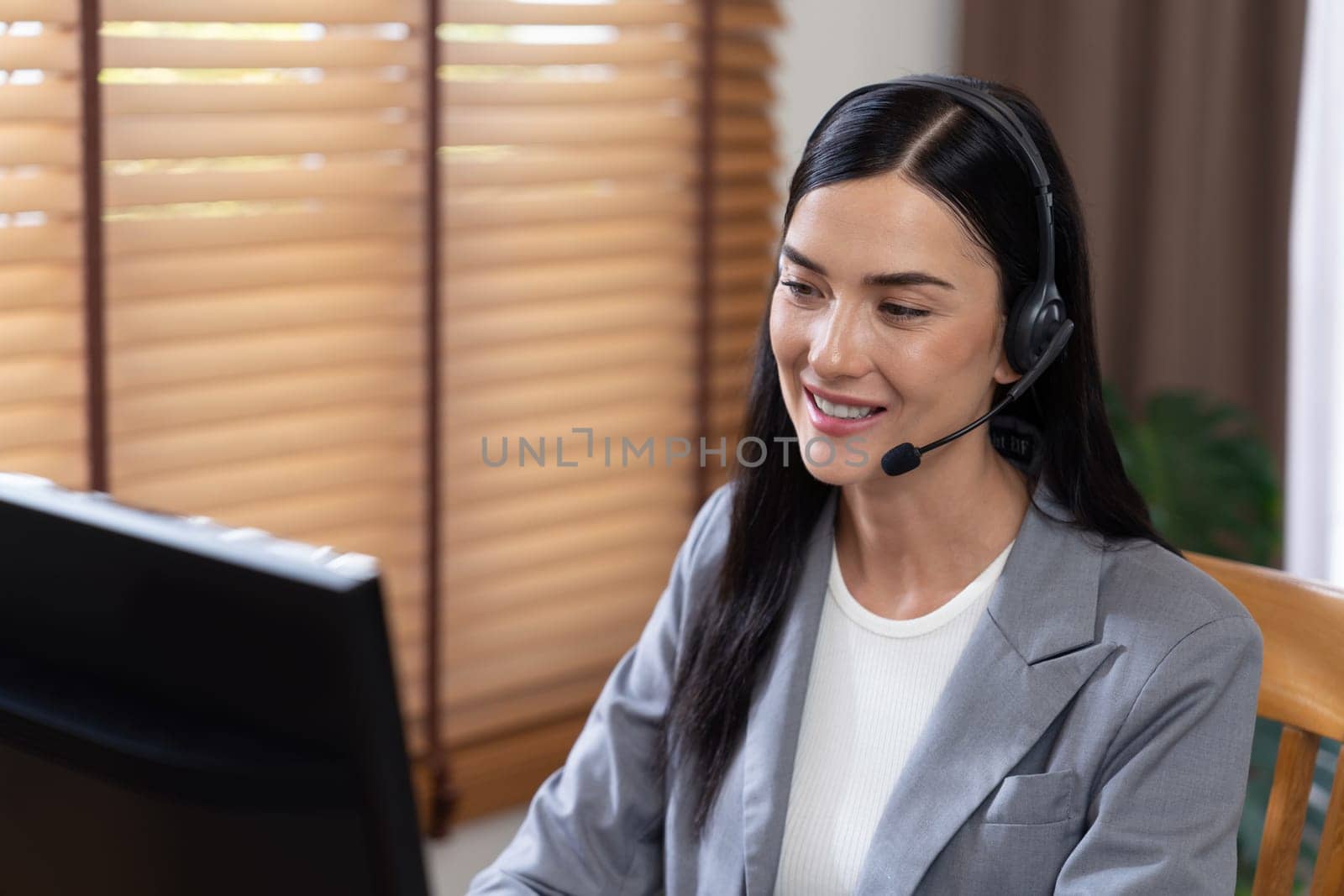 Female call center operator or customer service helpdesk staff working on workspace while talking on the headset to provide assistance for customer. Professional modern business service. Blithe