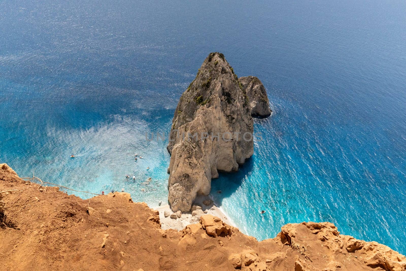 Beautiful view of a lonely cliff with a rocky beach and floating boats in the blue sea on a sunny summer day, top view from the mountain, close-up.