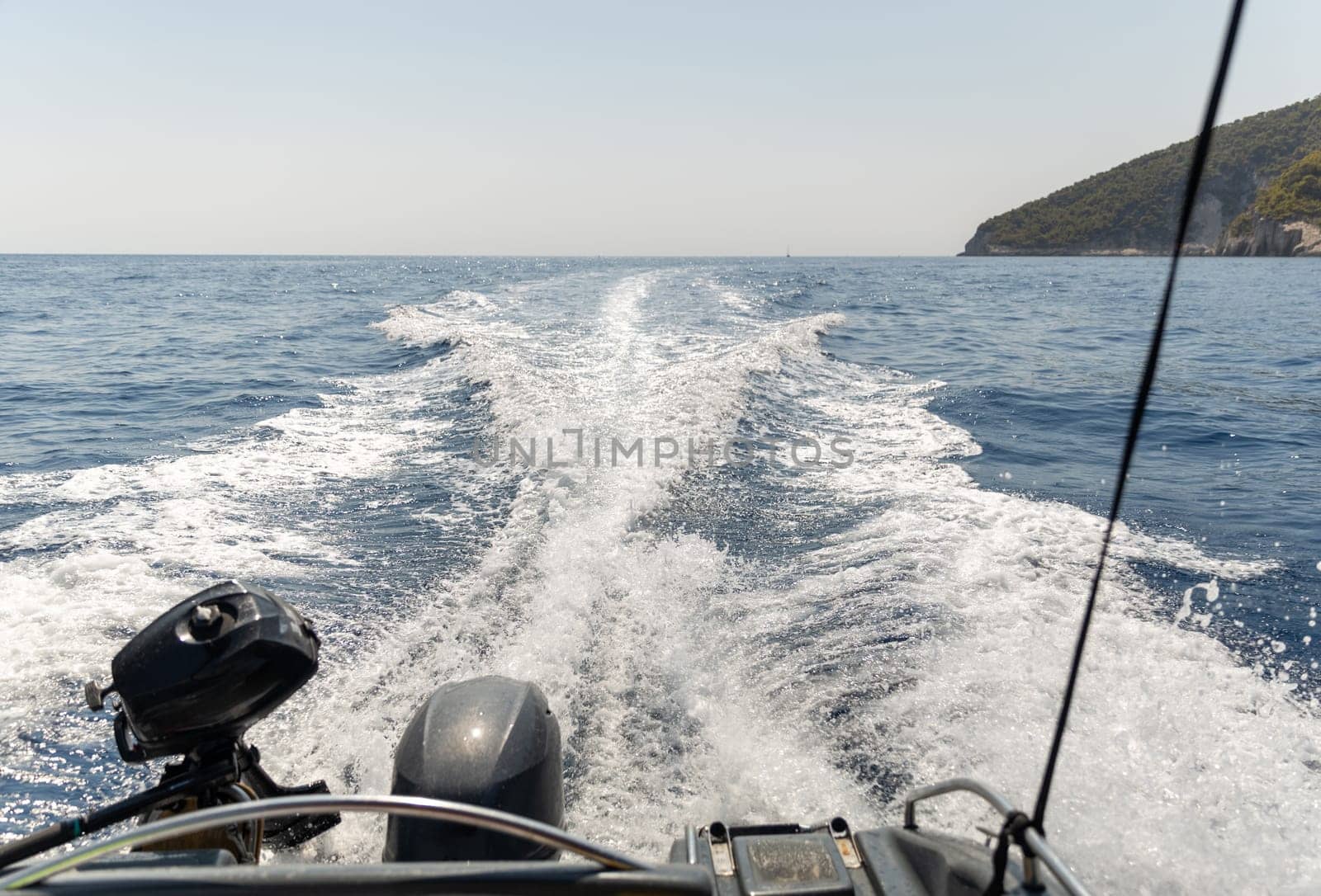 Beautiful view of the foaming furrows from a motor boat sailing on the blue sea around the island on a sunny summer day, close-up side view.