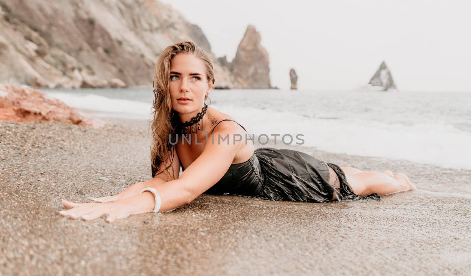 Woman travel sea. Young Happy woman in a long red dress posing on a beach near the sea on background of volcanic rocks, like in Iceland, sharing travel adventure journey