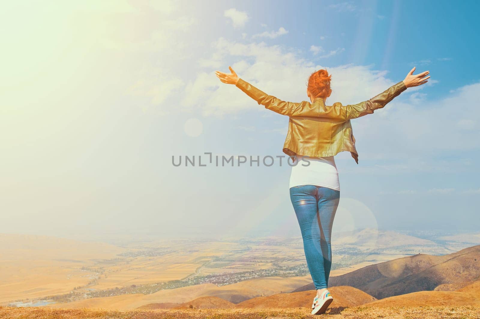 Woman in the mountain standing in the distance with her back to the camera and her arms outspread in celebration of a beautiful sunny summer day and freedom spread arms