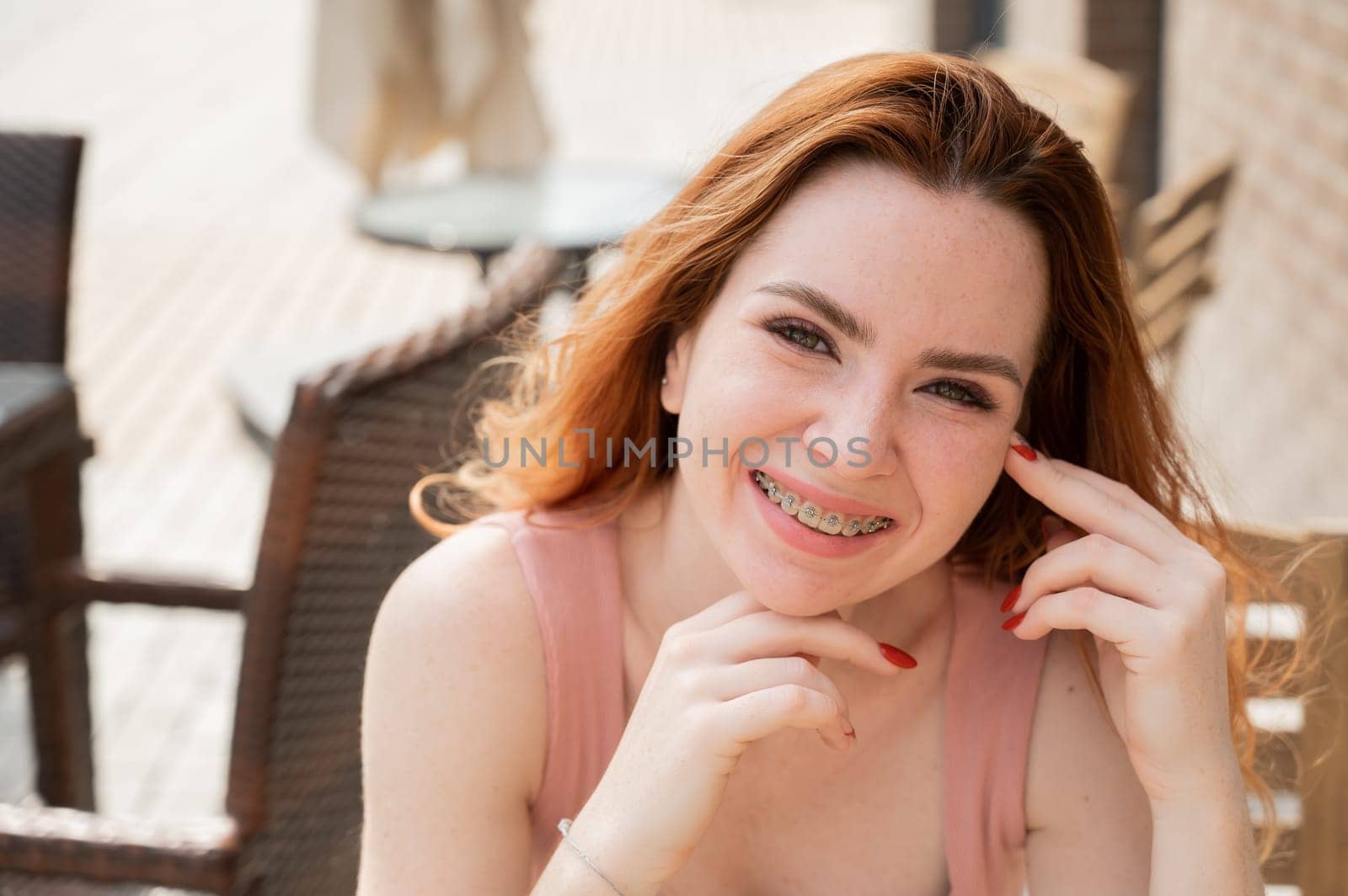Beautiful young red-haired woman with braces on her teeth smiling while sitting in an outdoor cafe
