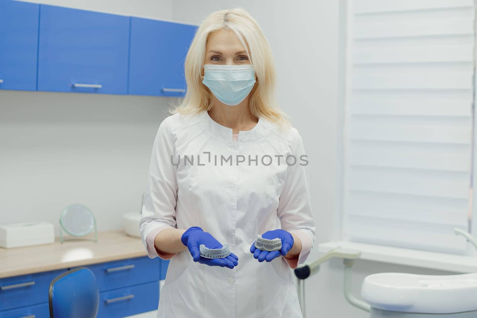 Woman working in dental clinic with patient sitting in chair and doctor in background.