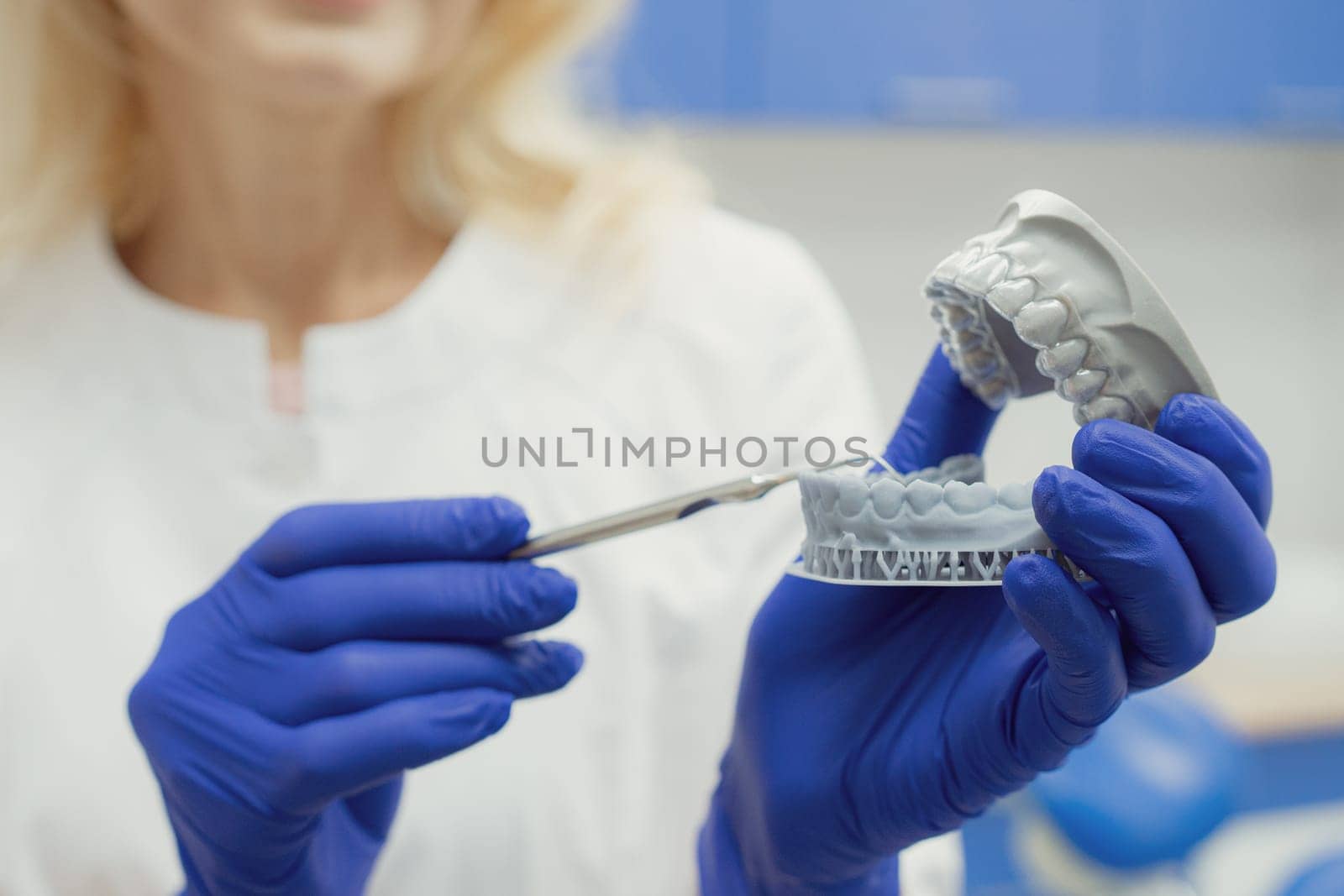 Woman working in dental clinic with patient sitting in chair and doctor in background.