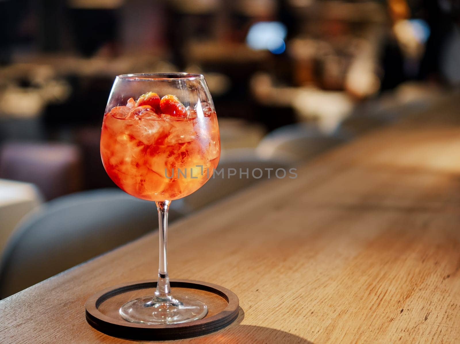 Transparent pink alcohol cocktail in wine glass with ice, aperol and gin on bar counter in restaurant interior. Alcohol drink Aperol Spritz aperitif cocktail. Cold alcoholic cocktail in bar or nightclub. Copy space