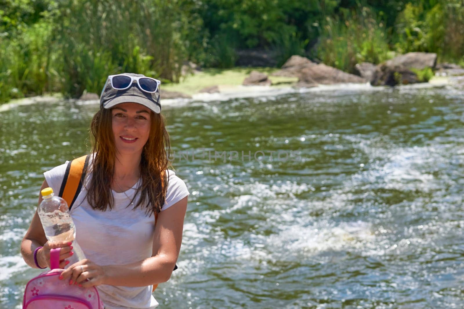 Young woman tourist with with a bottle of mineral water.Bank of a rapid river by jovani68