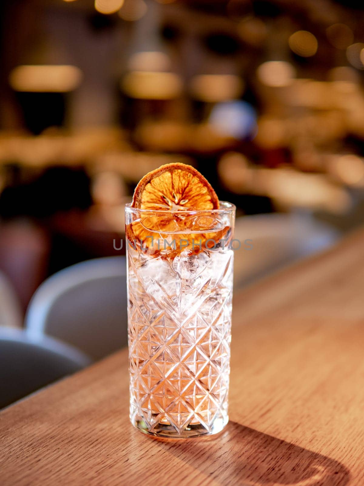 Transparent pink alcohol cocktail with ice, vodka and gin-tonic on bar counter in restaurant interior. Alcohol cocktail decorated orange slice. Cold alcoholic cocktail in bar or nightclub. Copy space