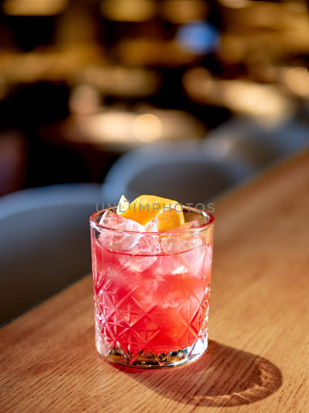 Transparent pink alcohol cocktail with ice, aperol and gin on bar counter in restaurant interior. Alcohol cocktail decorated orange zest spiral. Cold alcoholic cocktail in bar or nightclub. Copy space