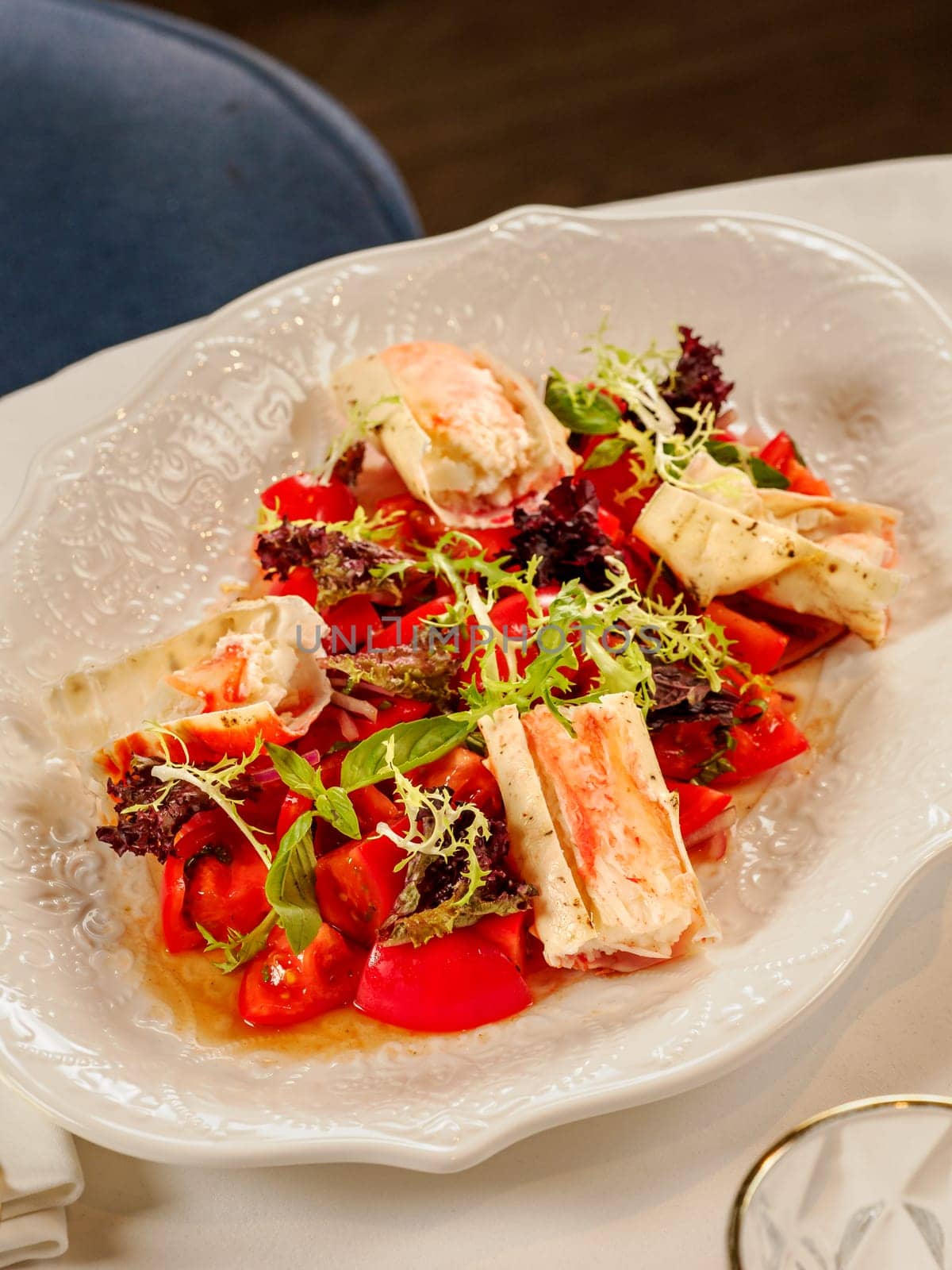Delicious seafood crab salad on white plate on restaurant table background. Plate with healthy salad made with crab, tomatoes and fresh greens, decorated basil