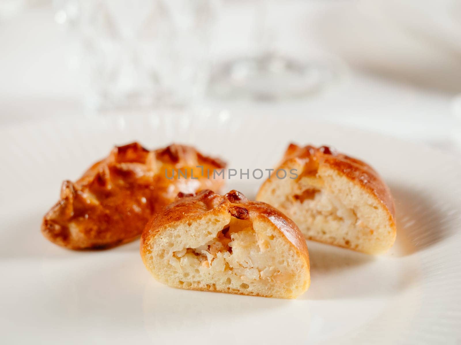 Small russian pies with minced salmon fish Russian Piroshki. Cooked tuna fish hand portioned pies or empanadas cut in half on white plate in elegant restaurant interior. Selective focus, close up.