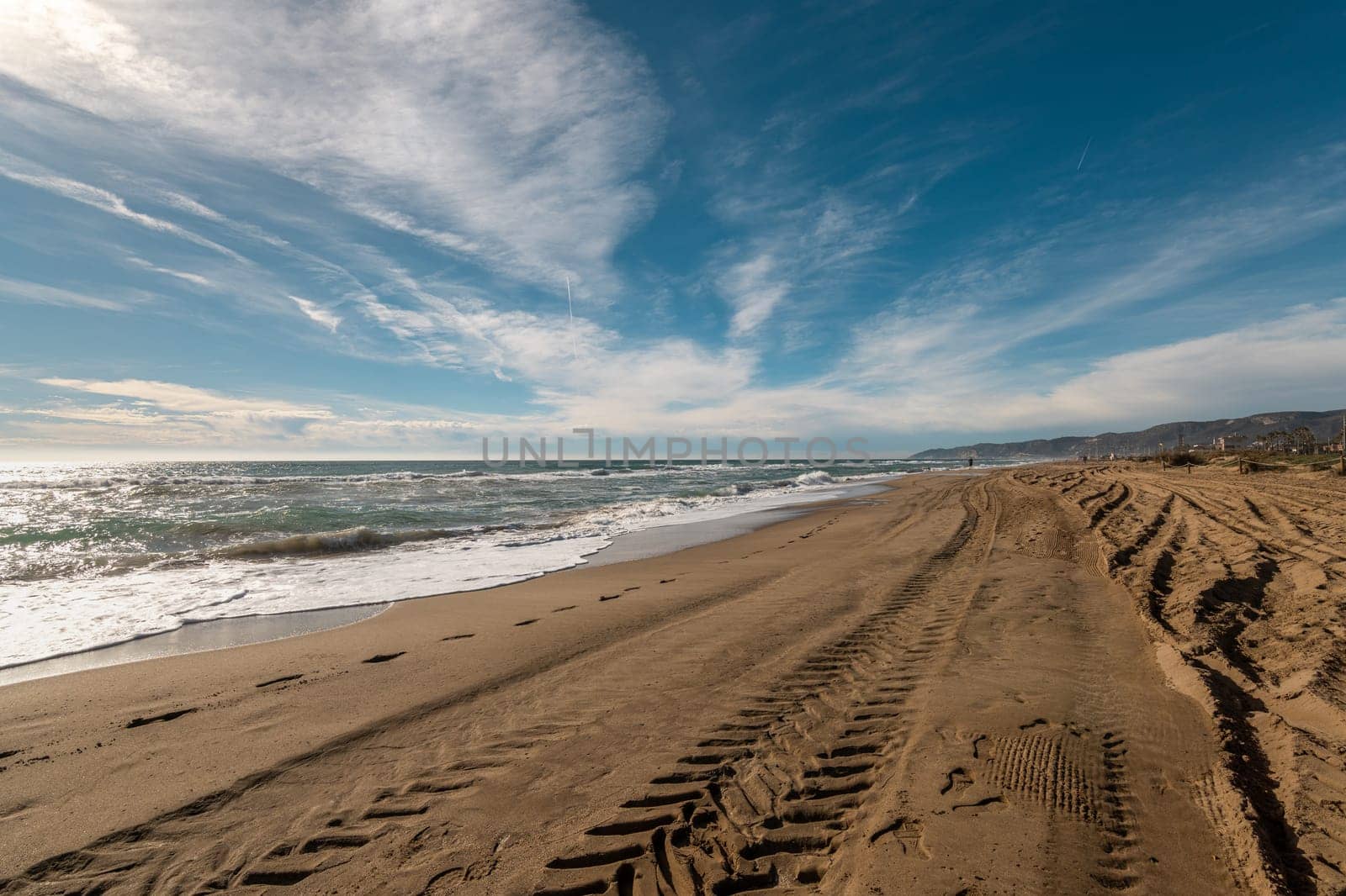 Expansive Sandy Shoreline with Tire Tracks Stretching Towards the Horizon Under Blue Skies by apavlin