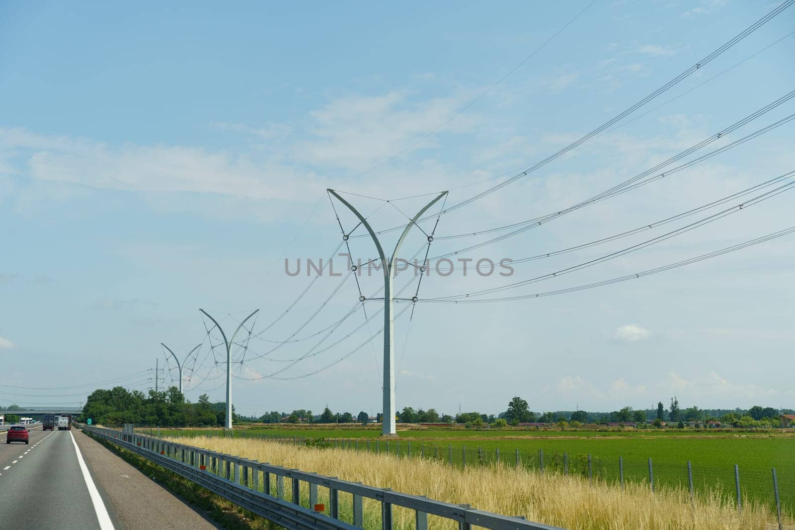 A car is seen driving down a highway next to a vast and vibrant green field under a clear blue sky.