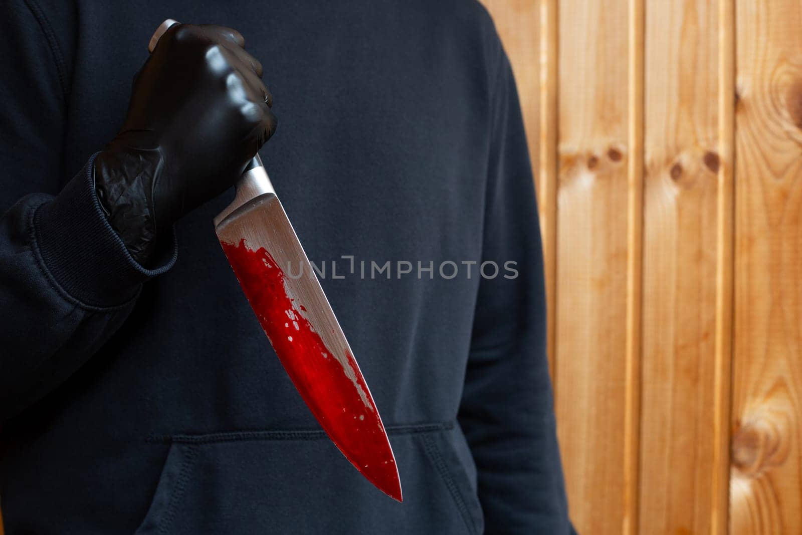 Maniac holds bloody knife with reverse grip, bloody sharp murder weapon in hands of killer in black clothes