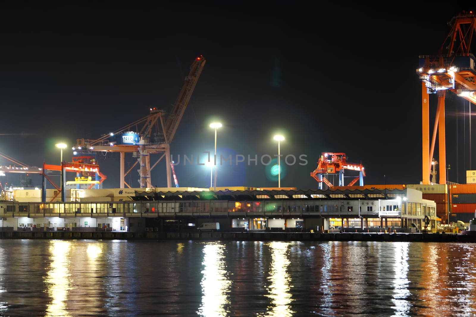 A large ship is docked at a pier with a large crane in the background