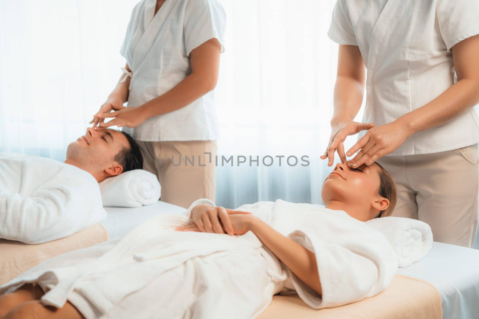 Caucasian couple enjoying relaxing anti-stress head massage and pampering facial beauty skin recreation leisure in dayspa modern light ambient at luxury resort or hotel spa salon. Quiescent